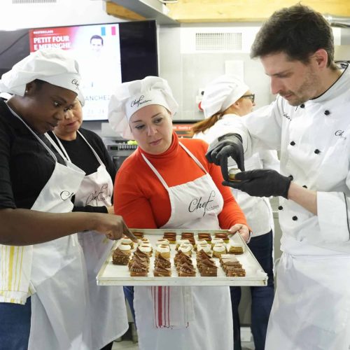 Masterclass di pasticceria alla Chef Academy: chef e allievi esaminano un vassoio di petit four e dolci al cioccolato
